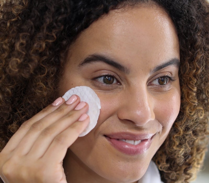 A woman applying a Neora Complexion Treatment Pad to her cheek.