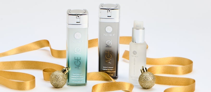 Neora’s Holiday Transformation Set which includes: Age IQ Day and Night Cream, SIG-1273 Serum alongside ornaments and gold ribbon