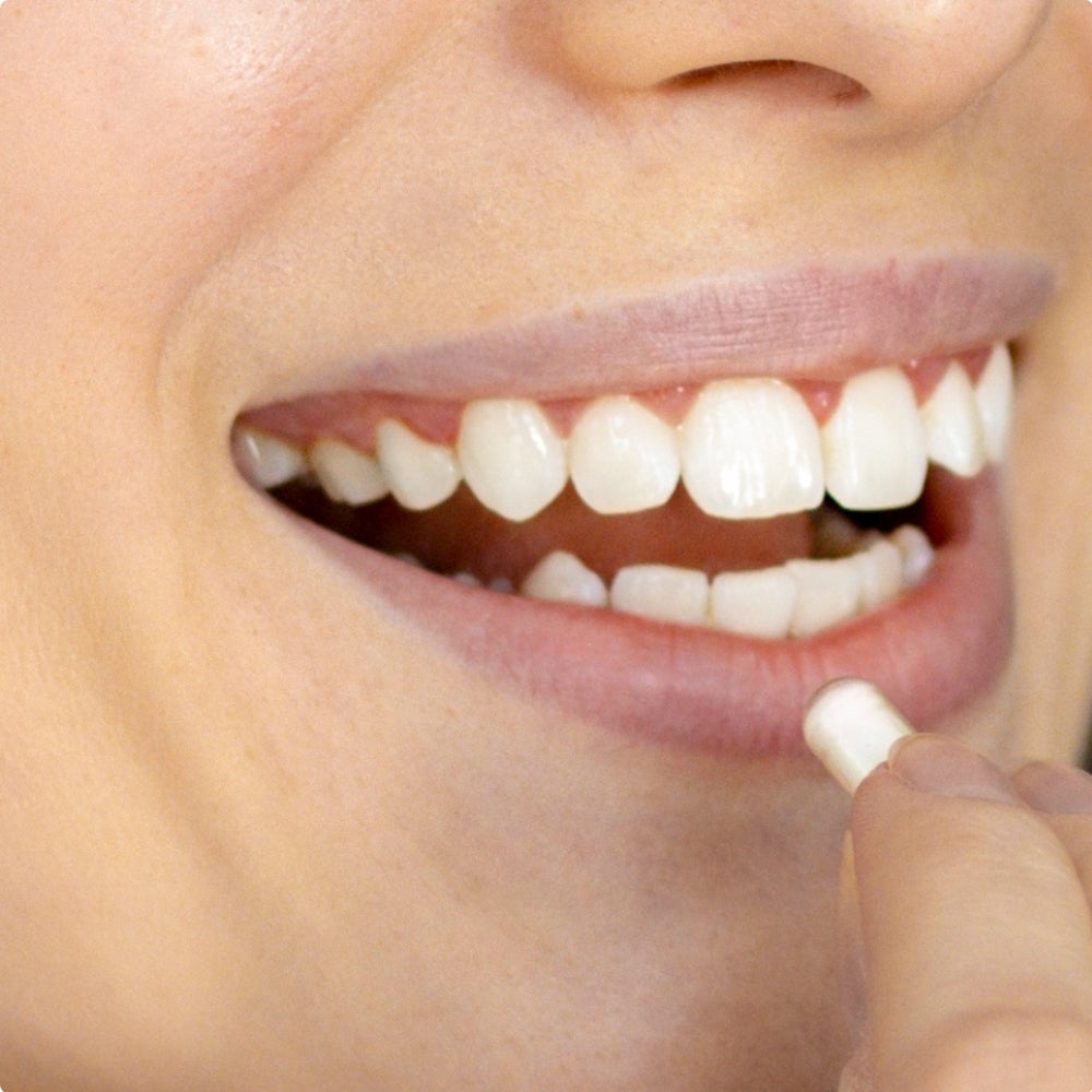 Image of woman smiling and placing a pill in her mouth