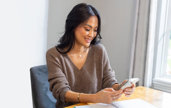 Image of woman sitting at a dining table and smiling while looking at her phone