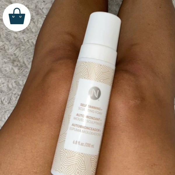 A woman holding a bottle of Sunless Tanner ontop of her legs.