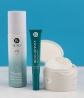 A combo of Neora’s Age IQ Double-Cleansing Face Wash, Moisture-Lock Lip Mask, and Complexion Clearing Pads on a white table in front of a teal background.