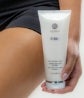 A seated woman holds a bottle of Firm Contour Cream next to her thigh.