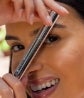 A woman holds up a tube of Neora’s LashLush Lash & Brow Serum closely to her face.