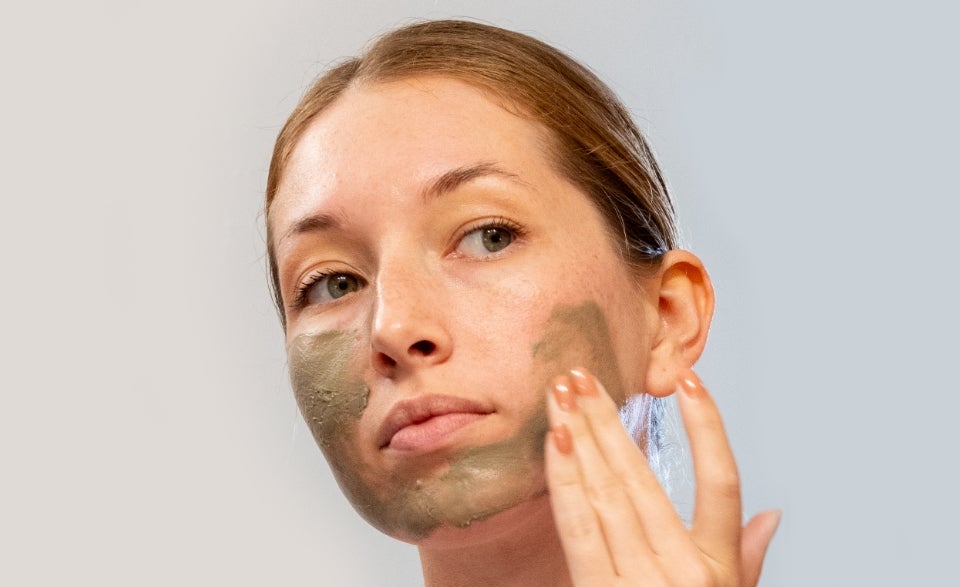 A woman smears Neora’s Clarifying Clay mask on her face.