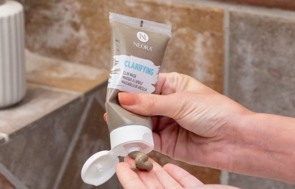 A woman dispenses product from a tube of Neora’s Clarifying Clay Mask in their hands.