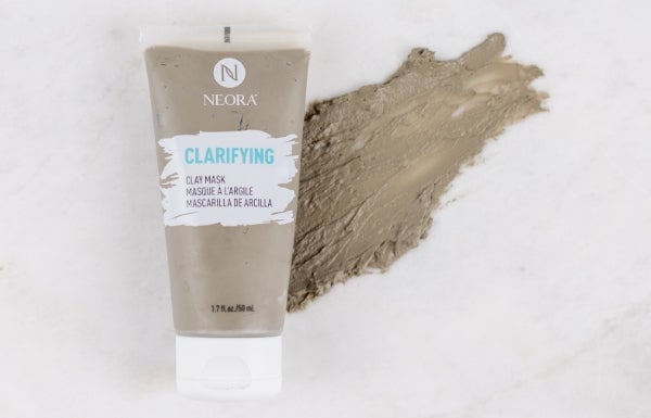 A tube of Neora’s Clarifying Clay Mask placed on a background with a smear of clay behind it.