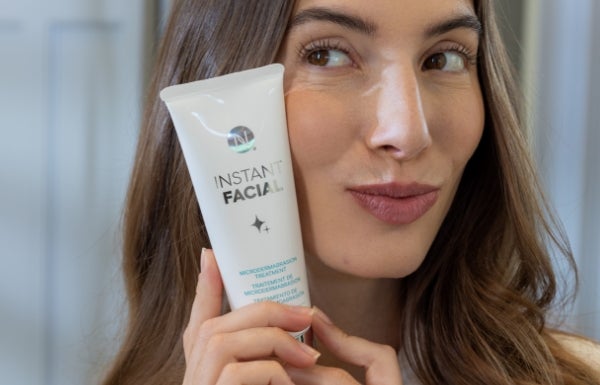 A close-up of a woman holding a tube of Instant Facial next to her face.