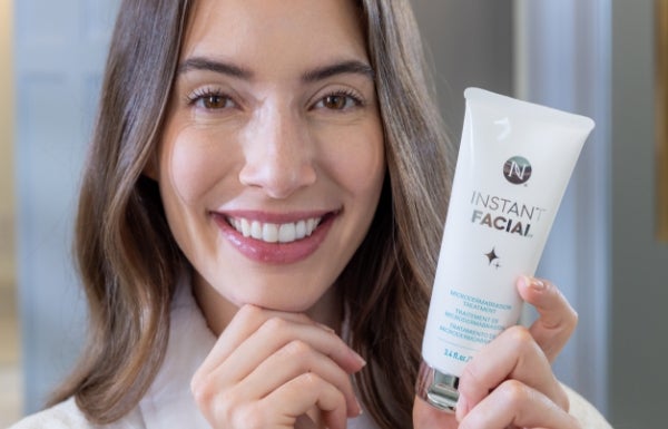 A close-up of a smiling woman holding a tube of Instant Facial next to her face.