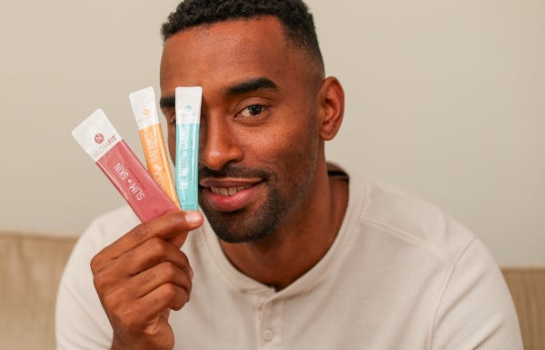 A man uses his right hand to hold NeoraFit sachets in front of part of his face.