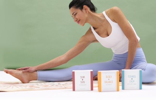 A woman stretches her leg while boxes of NeoraFit lay in front of her.