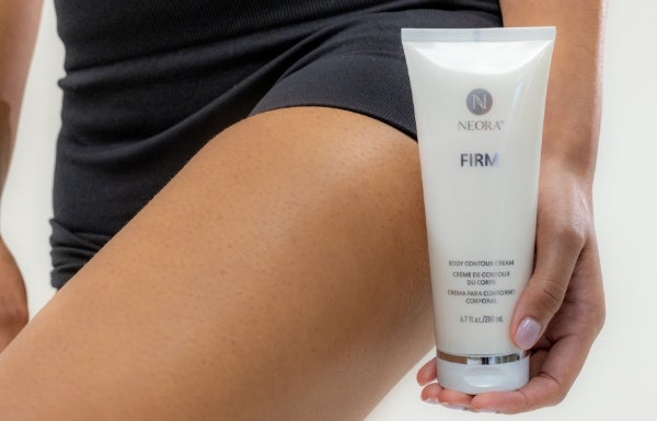 A woman holds a tube of Firm Body Contour Cream next to her thigh.