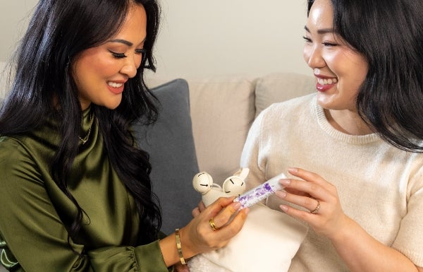 Two woman are smiling as they both hold a Neora’s Zen + Calm Lavender Balm between them.