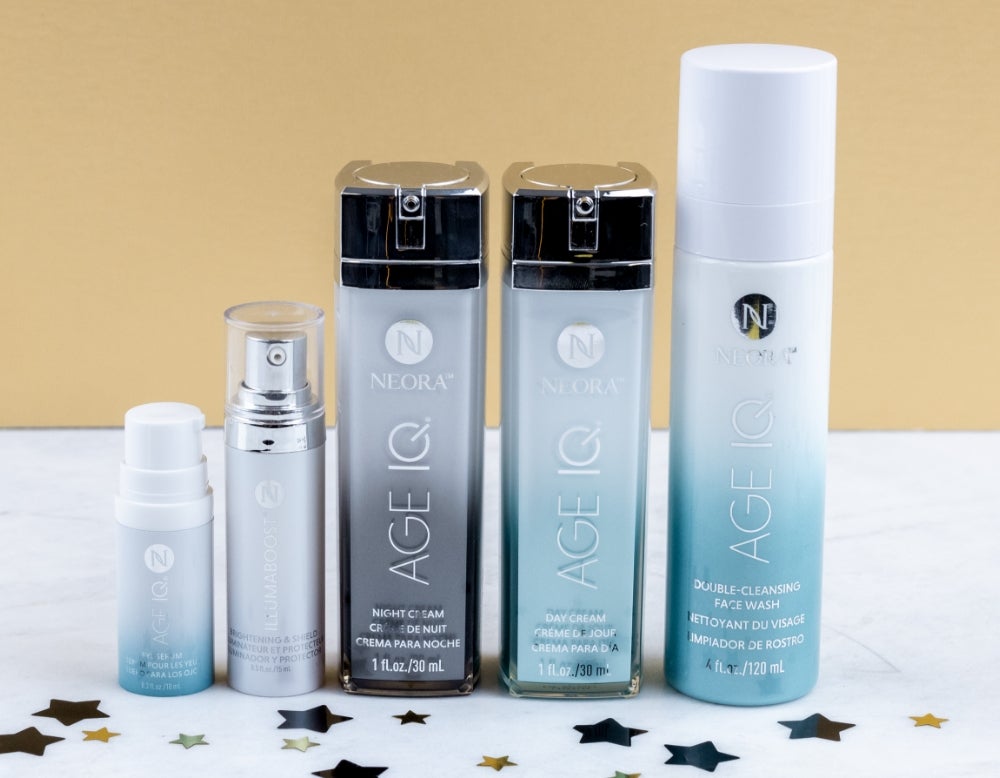 Neora’s Age IQ Eye Serum tube, IllumaBoost bottle, Age IQ Day and Night Cream bottles, Age IQ Double double-cleansing face wash all sit on a white marble table with glitter stars sounding them. And text that says “save 20%” and “free gift!