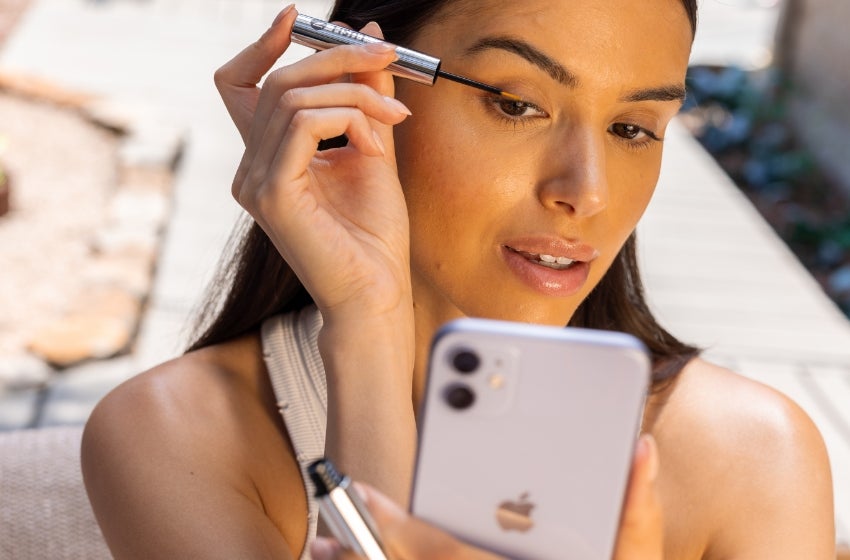 A woman uses her phone to help apply LashLush to her eyelashes.