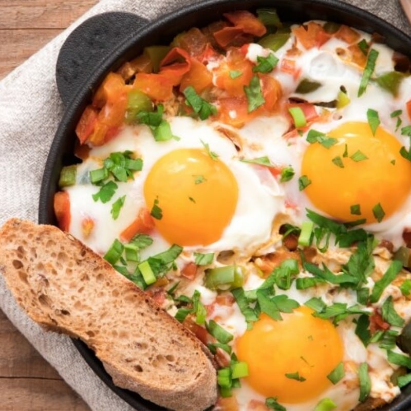 A skillet with eggs, tomatoes, and a piece of bread.