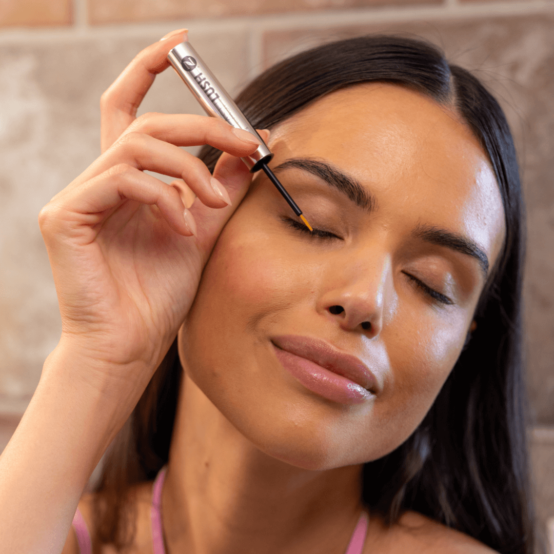 A face shot of a woman applying LashLush to her eyebrows.