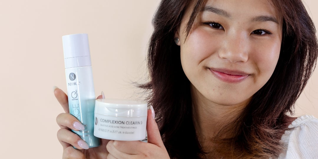 A teenage girl holding up Neora's Complexion Clearing Pads and Age IQ Double-Cleansing Face Wash.