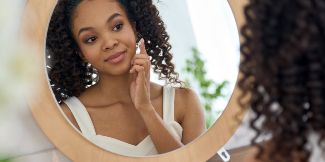 A woman applies moisturizer to her face.