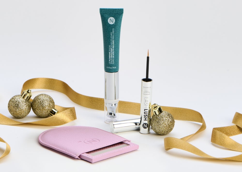 A Lip Plumping Serum and LashLush tube are surrounded by gold ribbon, ornaments and a pink purse mirror. Accompanying text states “Free Gift!” And “Save 15%.”